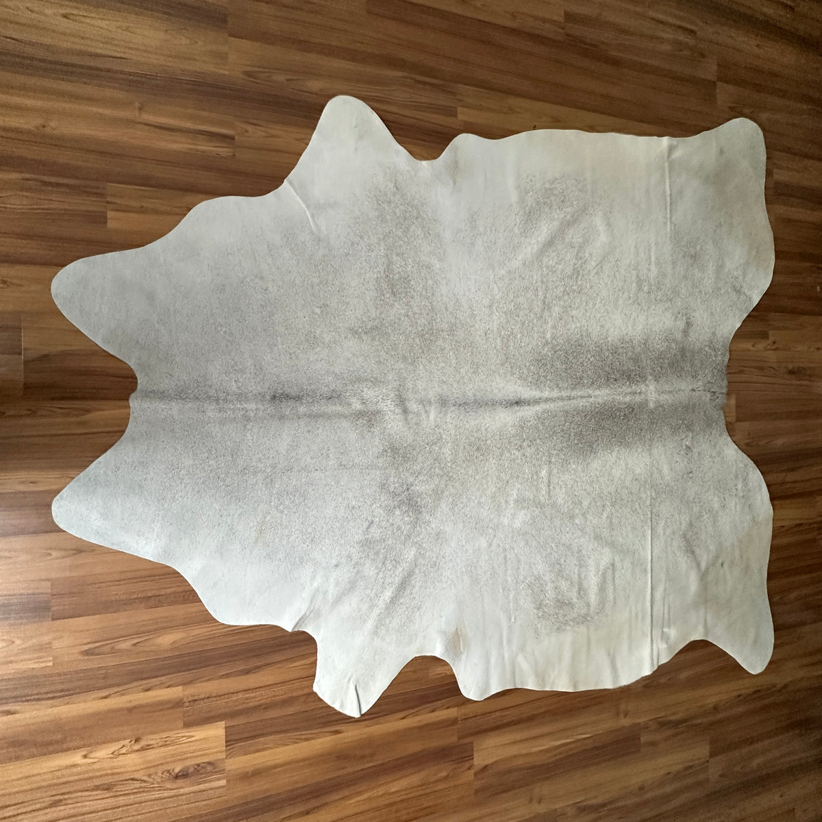Beige cowhide rug, full overhead view — Light cream base with subtle grey-brown natural markings and irregular patches