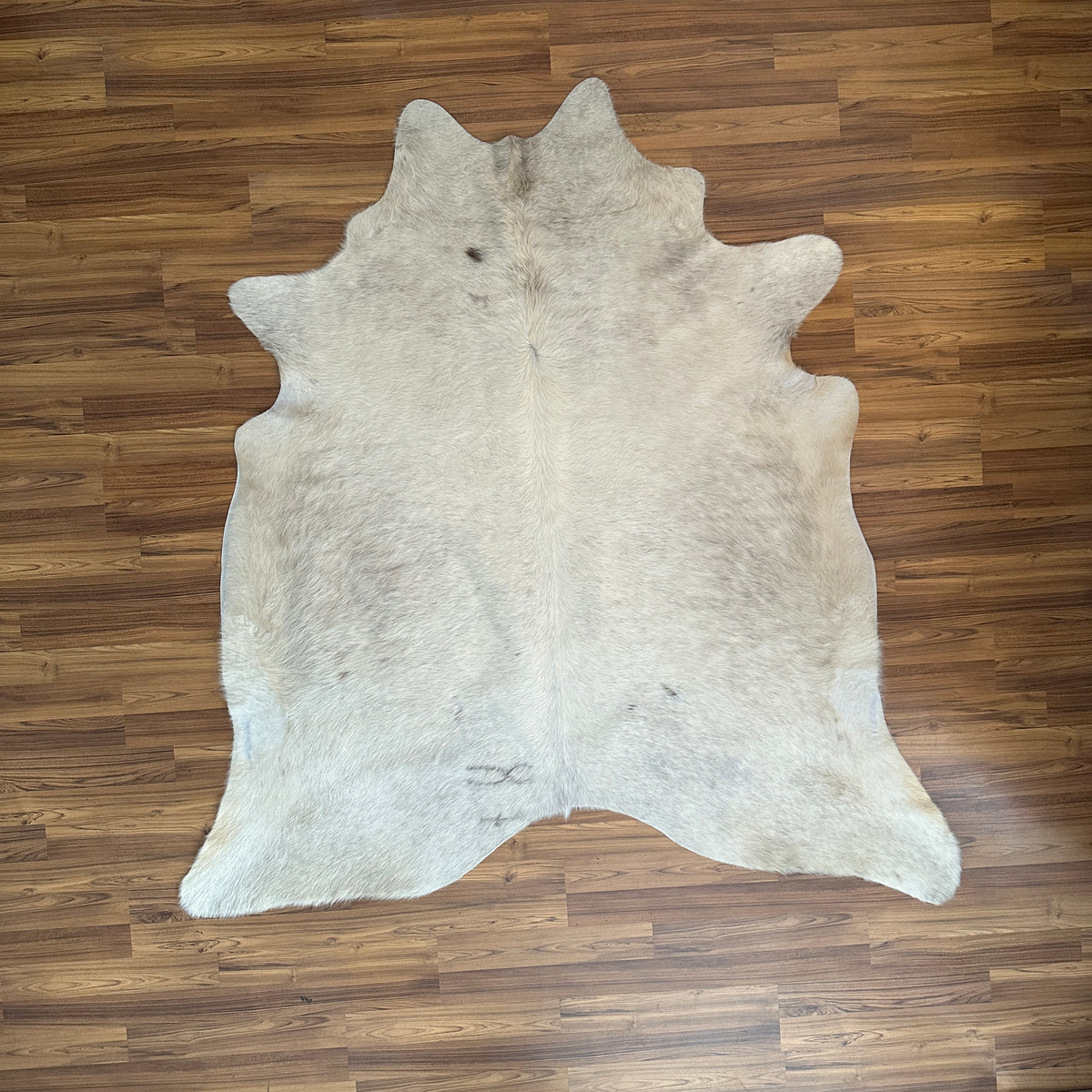 Beige cowhide rug, full overhead view — Fine cream base with scattered grey-brown markings and natural hide variations