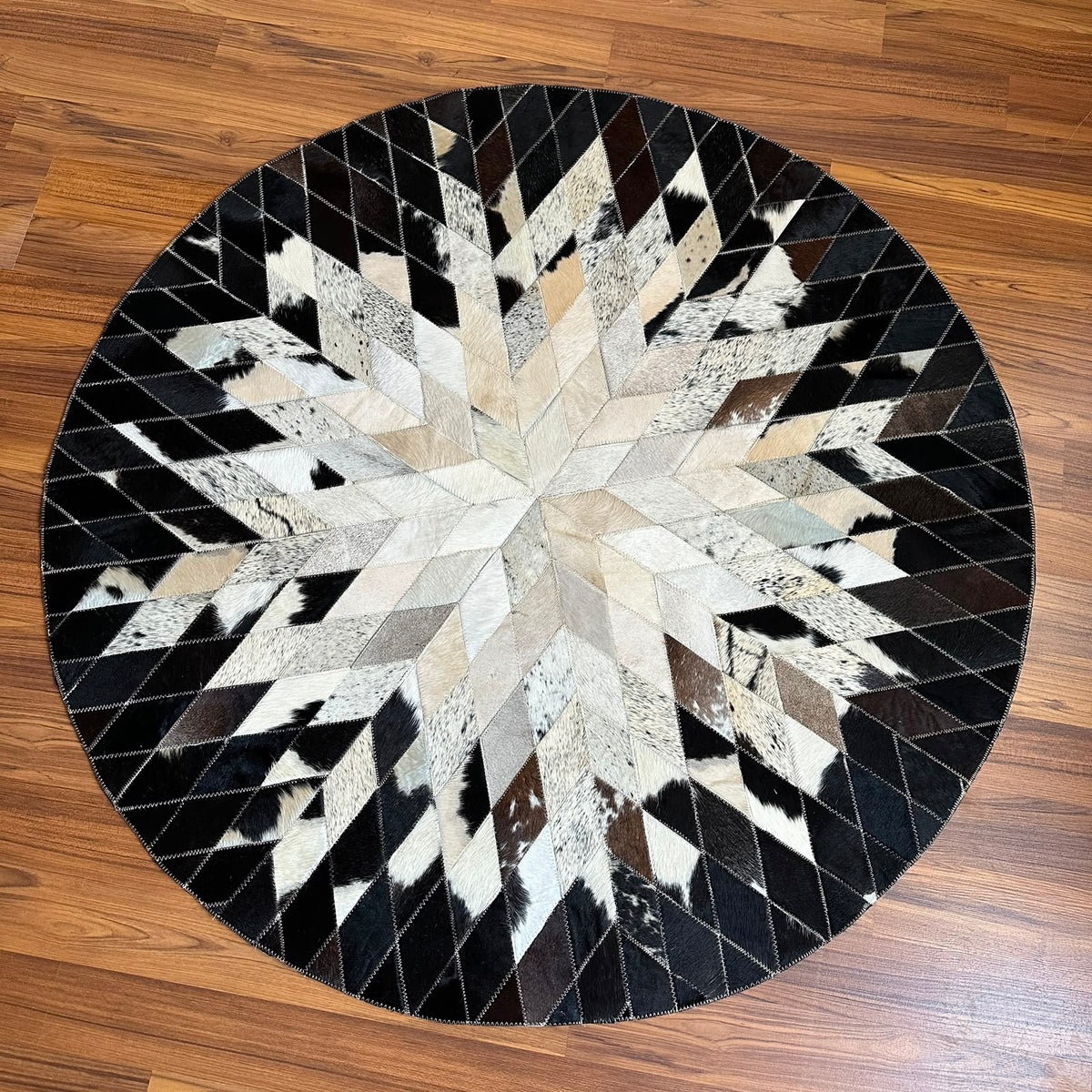 Black and White round patchwork cowhide rug, full overhead view — Geometric star burst design radiating from center, assemble