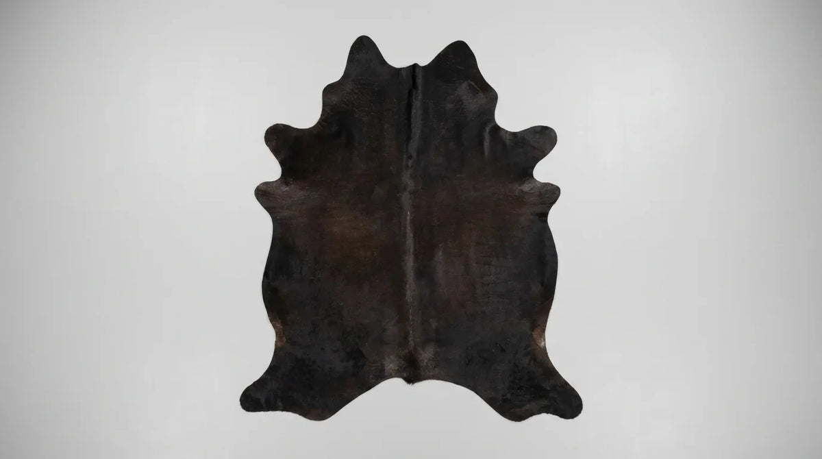 Black cowhide rug flat lay on white background showing full hide shape