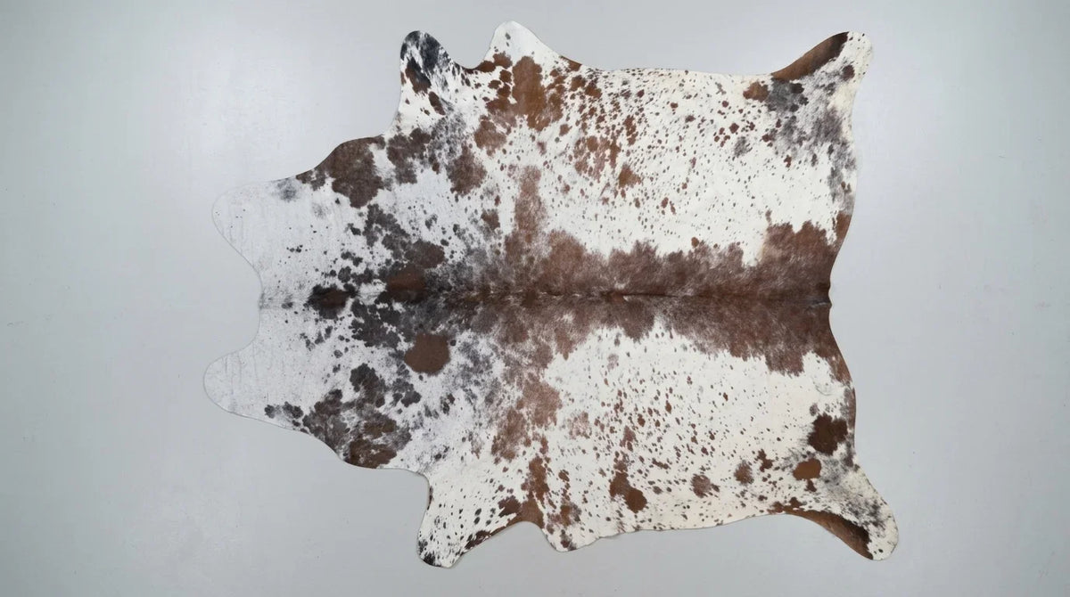 Brown and White cowhide rug flat lay on white background showing full hide shape
