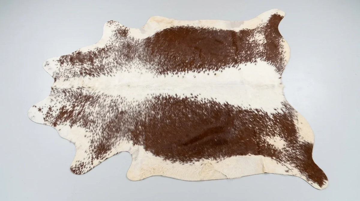 Brown and White cowhide rug flat lay on white background showing full hide shape