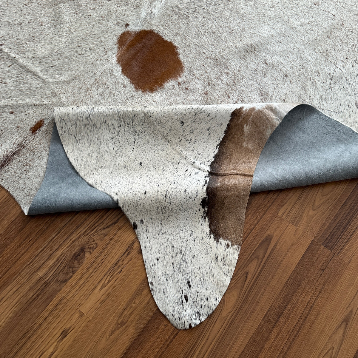 Close-up texture of Brown and White cowhide rug — Large irregular chocolate brown patches and smaller dark spots over cream b