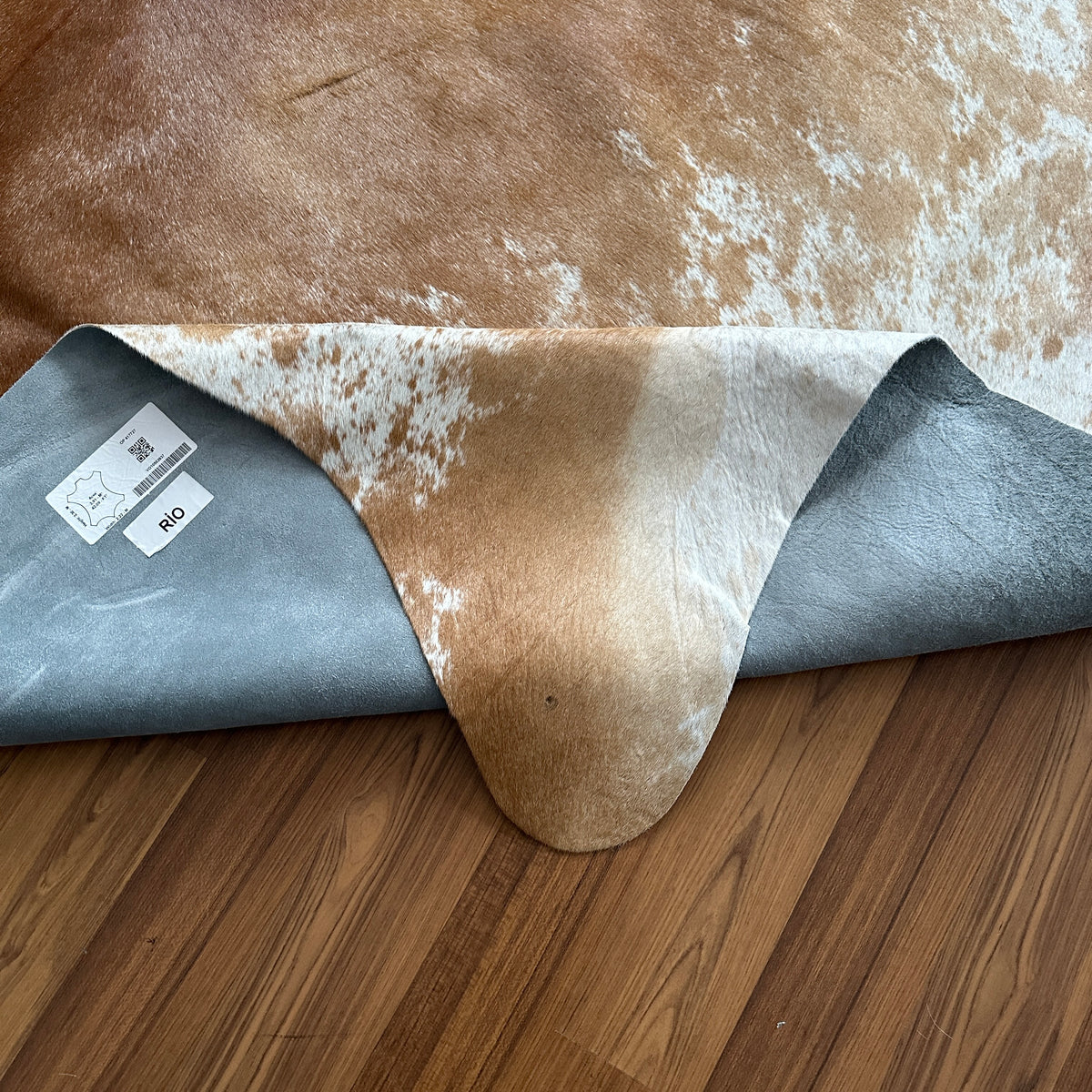 Close-up texture of Brown and White cowhide rug — Large irregular tan and cream patches with white speckled areas over warm b