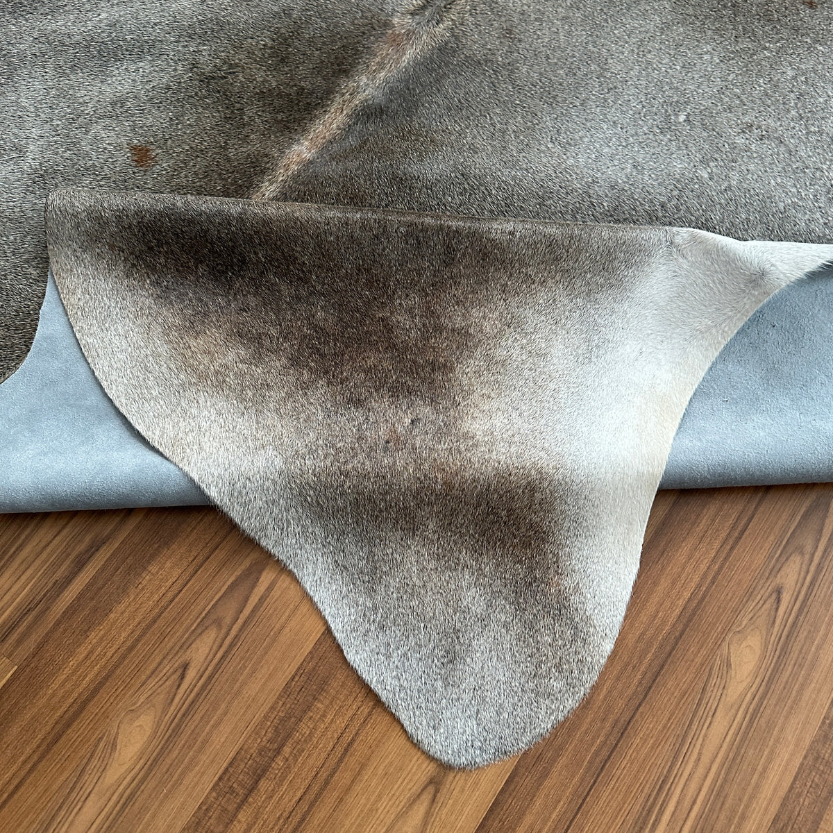 Close-up texture of Grey cowhide rug — Large irregular patches with warm brown undertones over light grey base