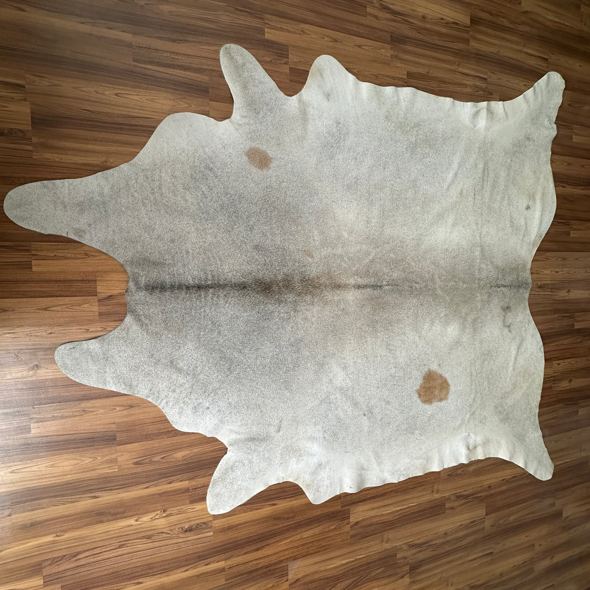 Beige cowhide rug, full overhead view — Light cream base with scattered faint tan patches and natural hide markings