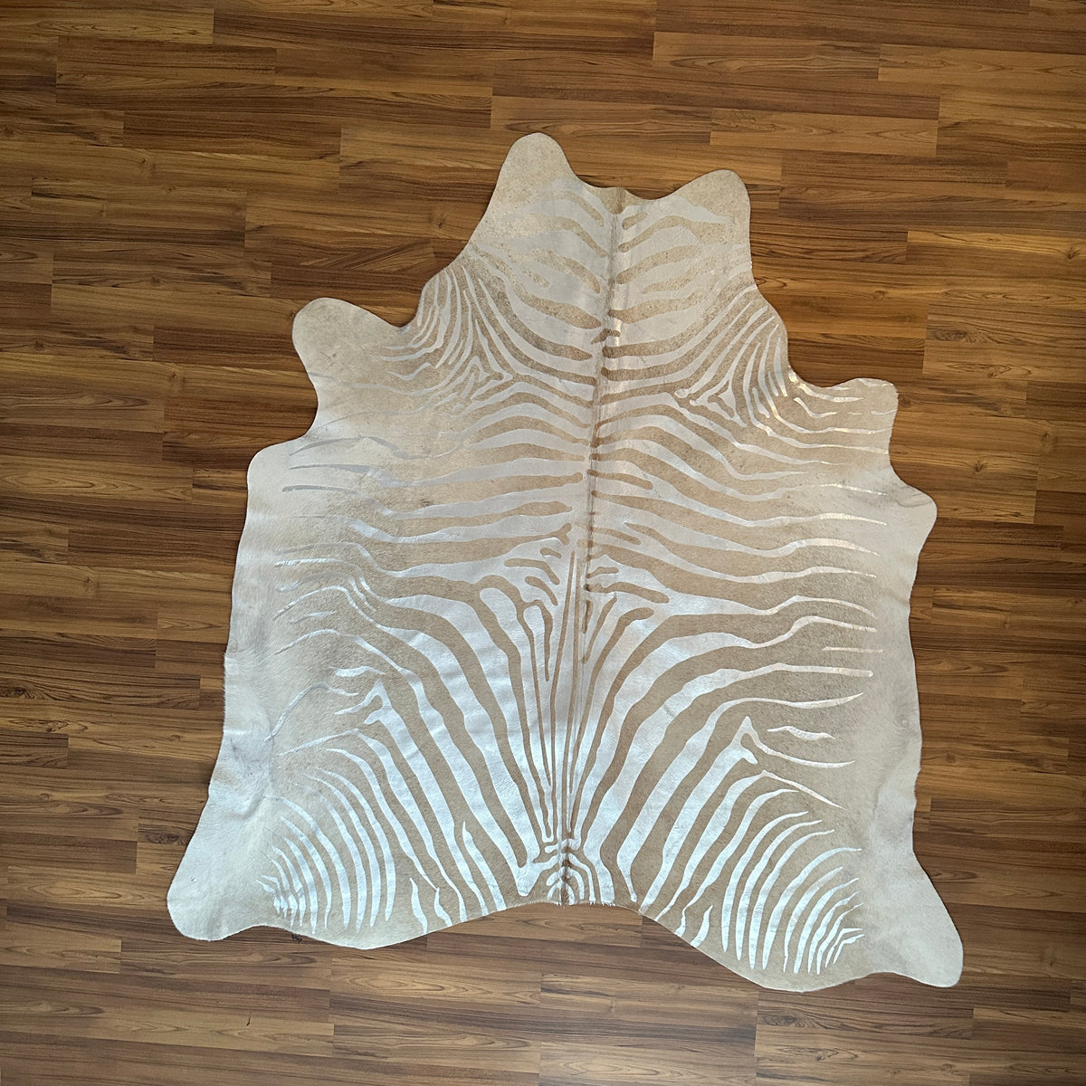 Beige zebra print cowhide rug, full overhead view — Bold radiating zebra stripes in warm tan and cream tones over light ivory