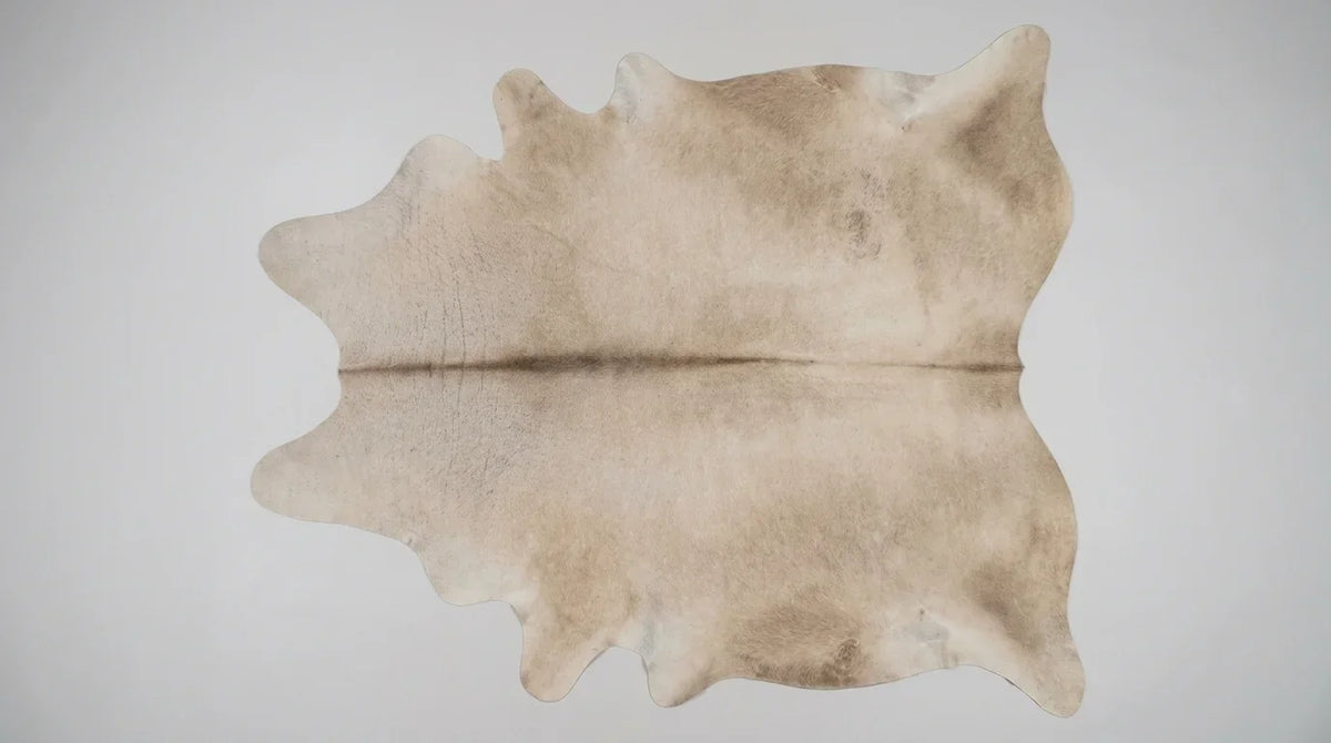 Beige cowhide rug flat lay on white background showing full hide shape