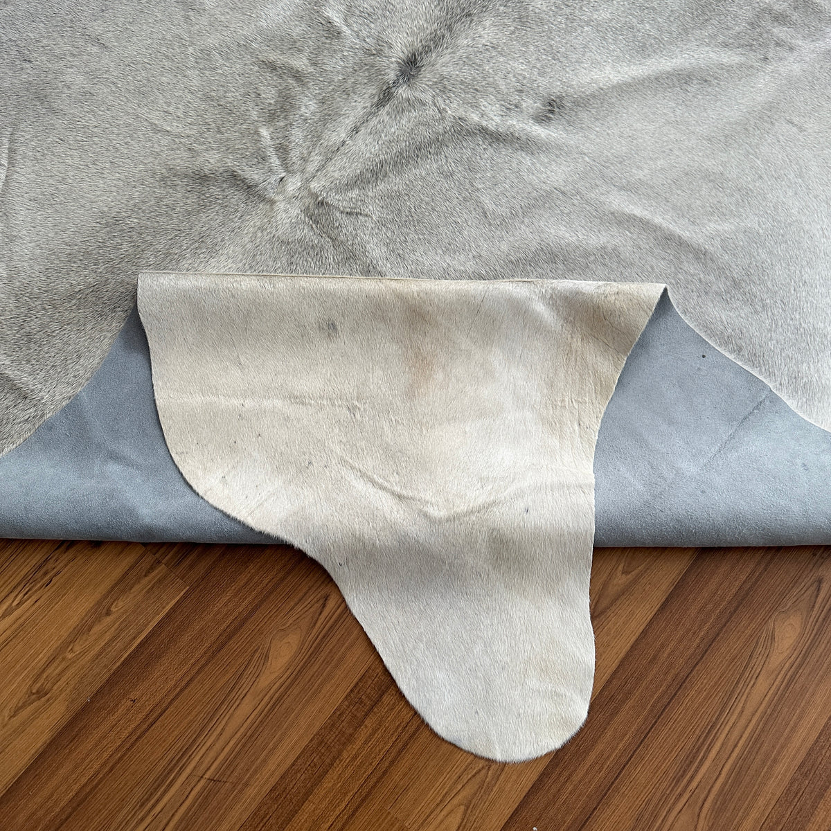 Close-up texture of Beige cowhide rug — Large irregular cream and grey patches with subtle charcoal markings