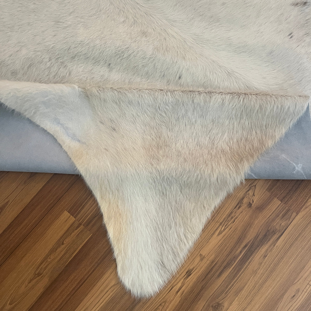 Close-up texture of Beige cowhide rug — Fine cream base with scattered grey-brown markings and natural hide variations