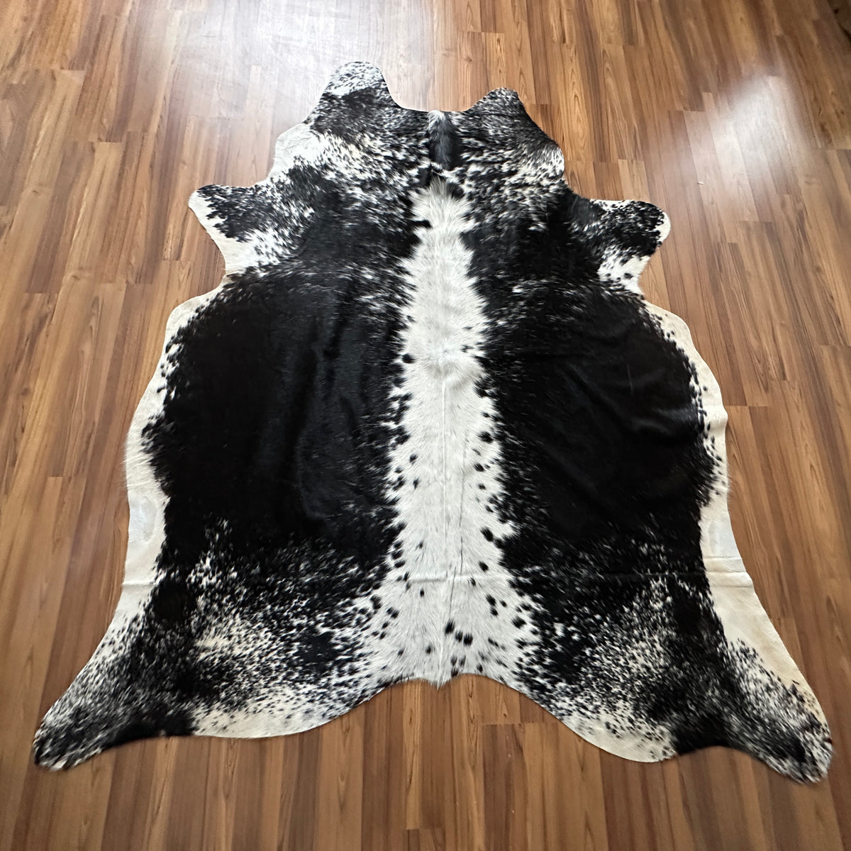 Black and White cowhide rug, full overhead view — Large irregular black patches with white base and central white stripe