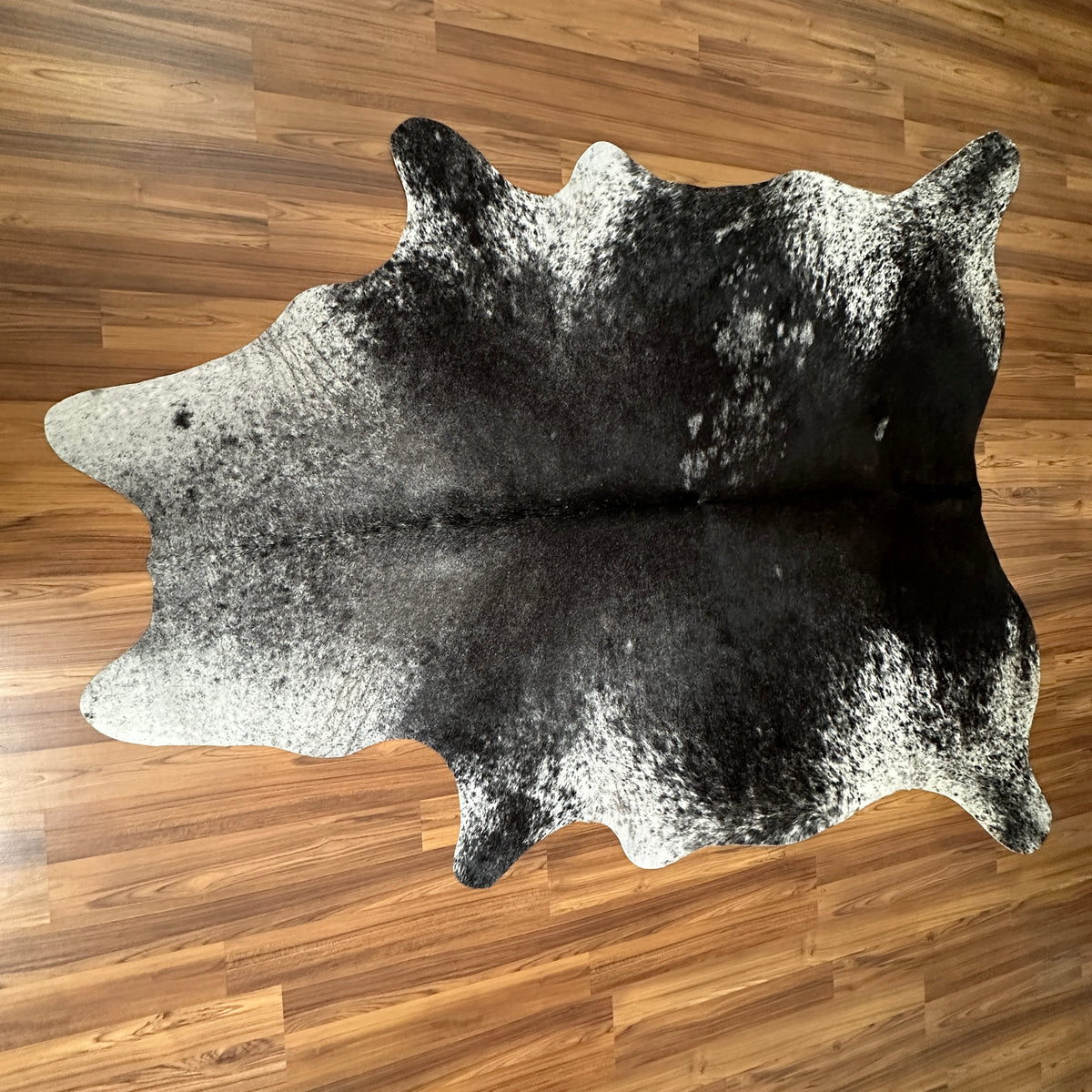 Black and White cowhide rug, full overhead view — Large irregular black and white patches with salt-and-pepper speckle textur