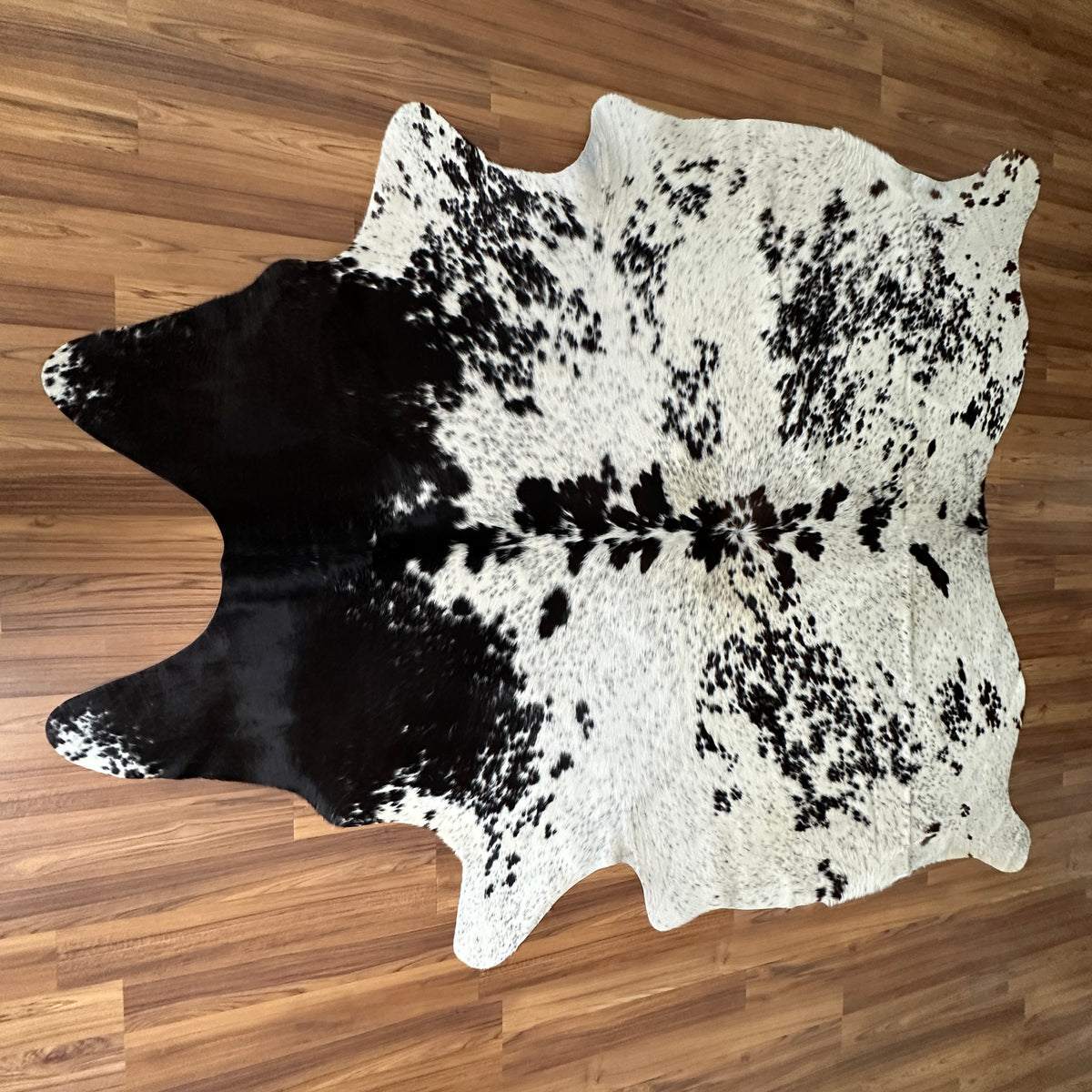 Black and White cowhide rug, full overhead view — Large irregular black patches over white cream base with fine speckled mark