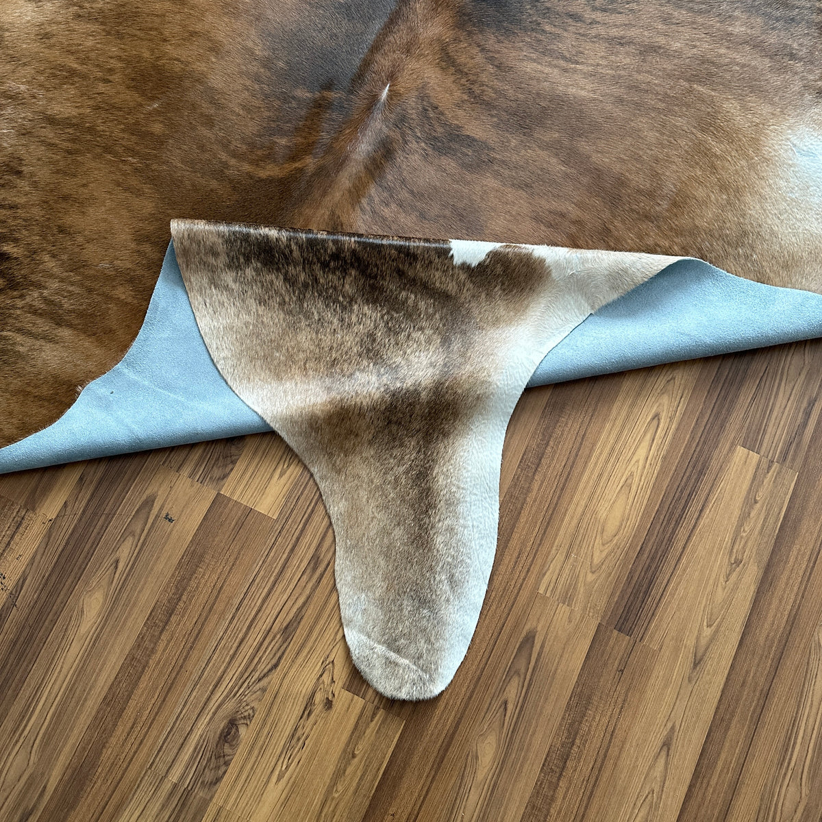 Close-up texture of Brown and White cowhide rug — Large irregular brown patches with cream and white accent areas over a ligh
