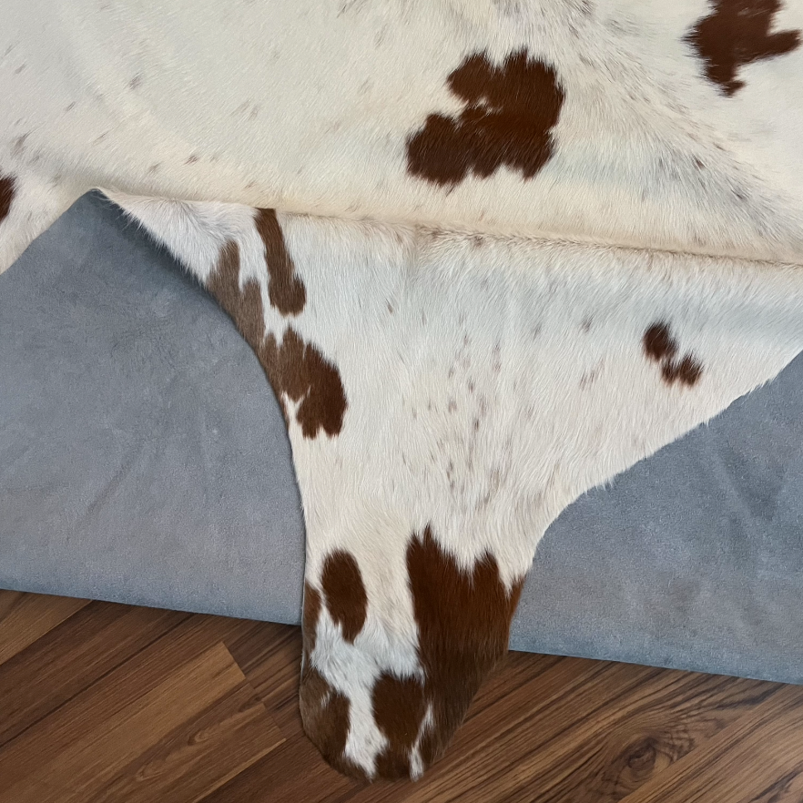 Close-up texture of Brown and White cowhide rug — Large irregular chocolate-brown patches and speckles scattered across a cre