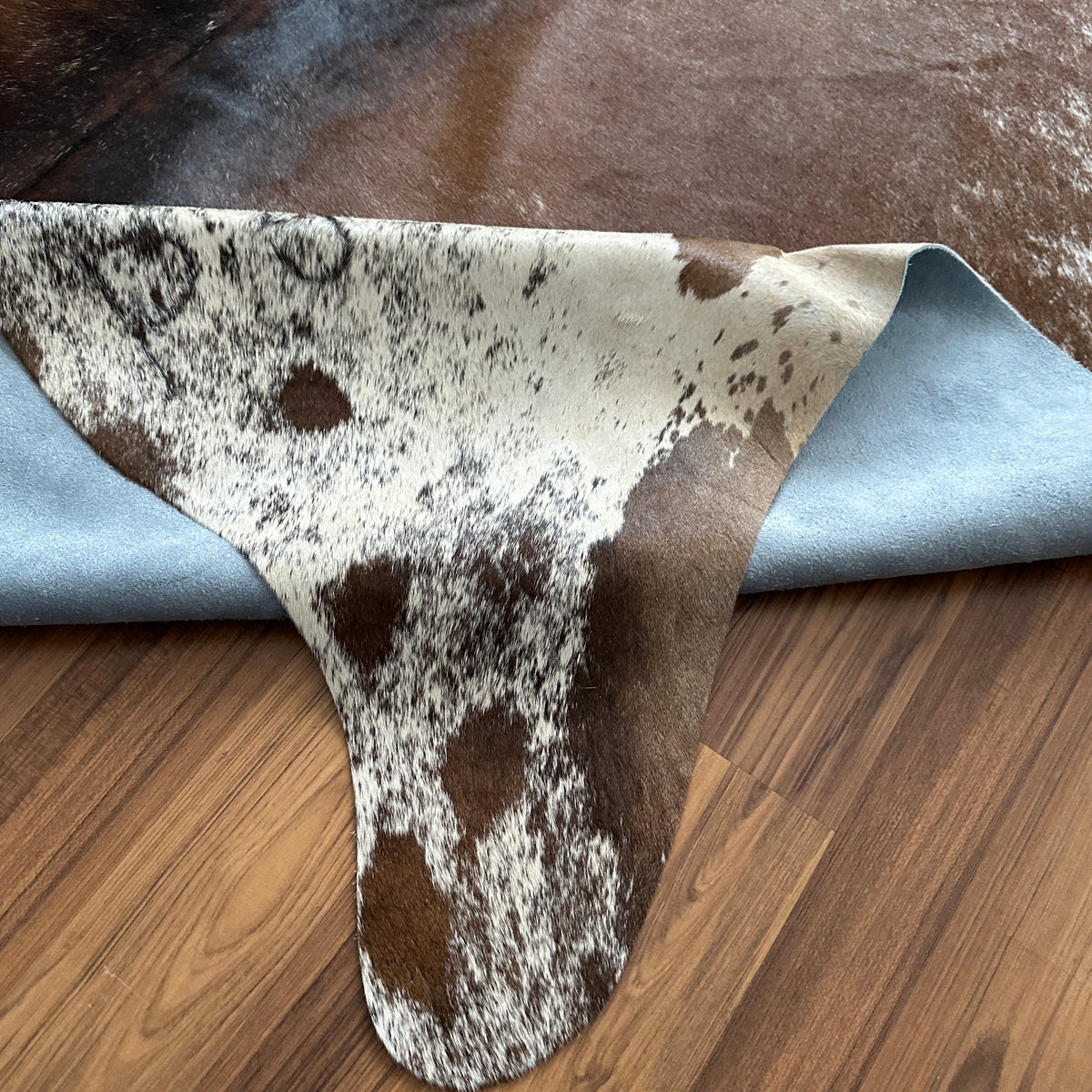 Close-up texture of Brown and White cowhide rug — Large irregular dark brown patches over creamy white base with scattered sp