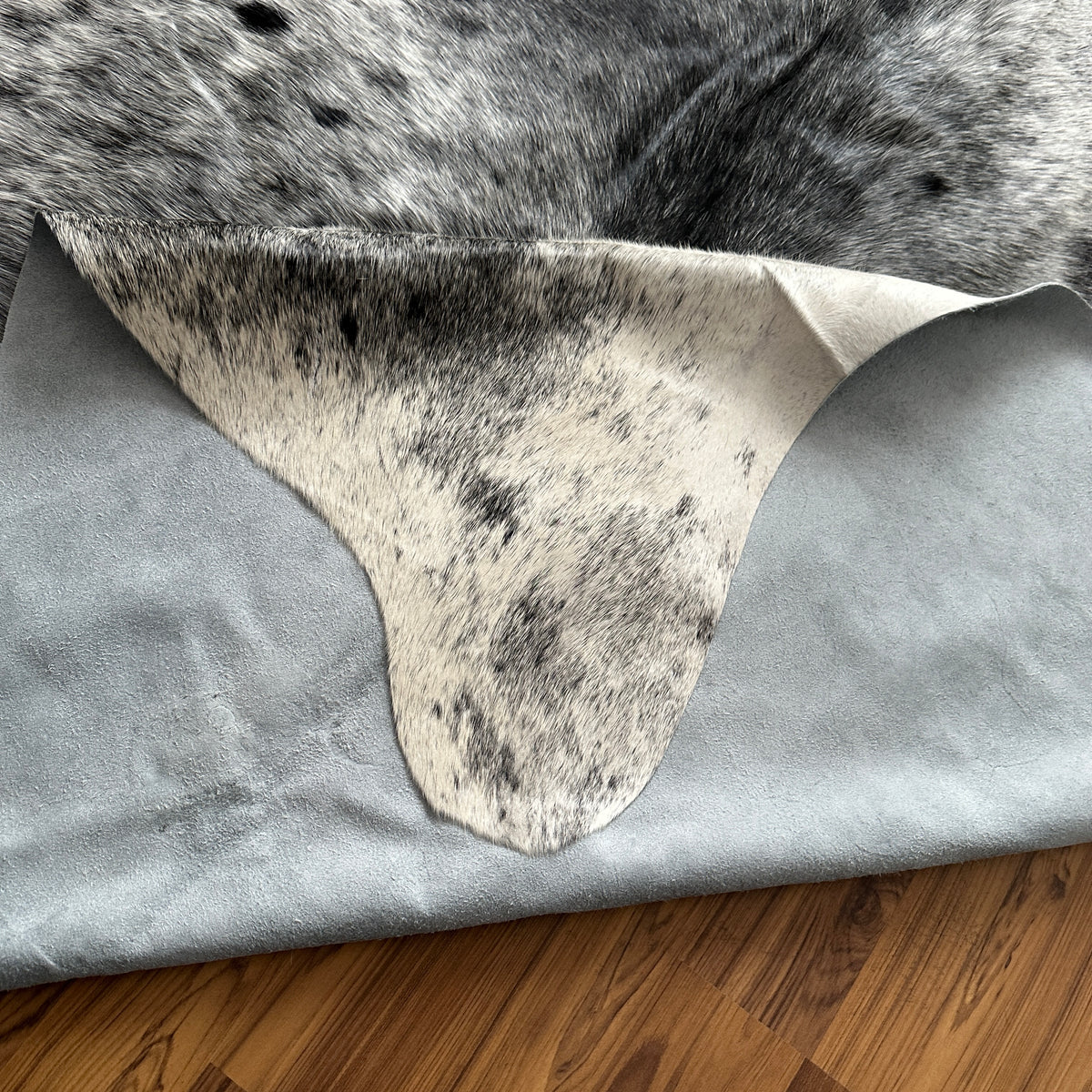 Close-up texture of Grey cowhide rug — Fine salt and pepper speckle with darker grey patches over light cream base