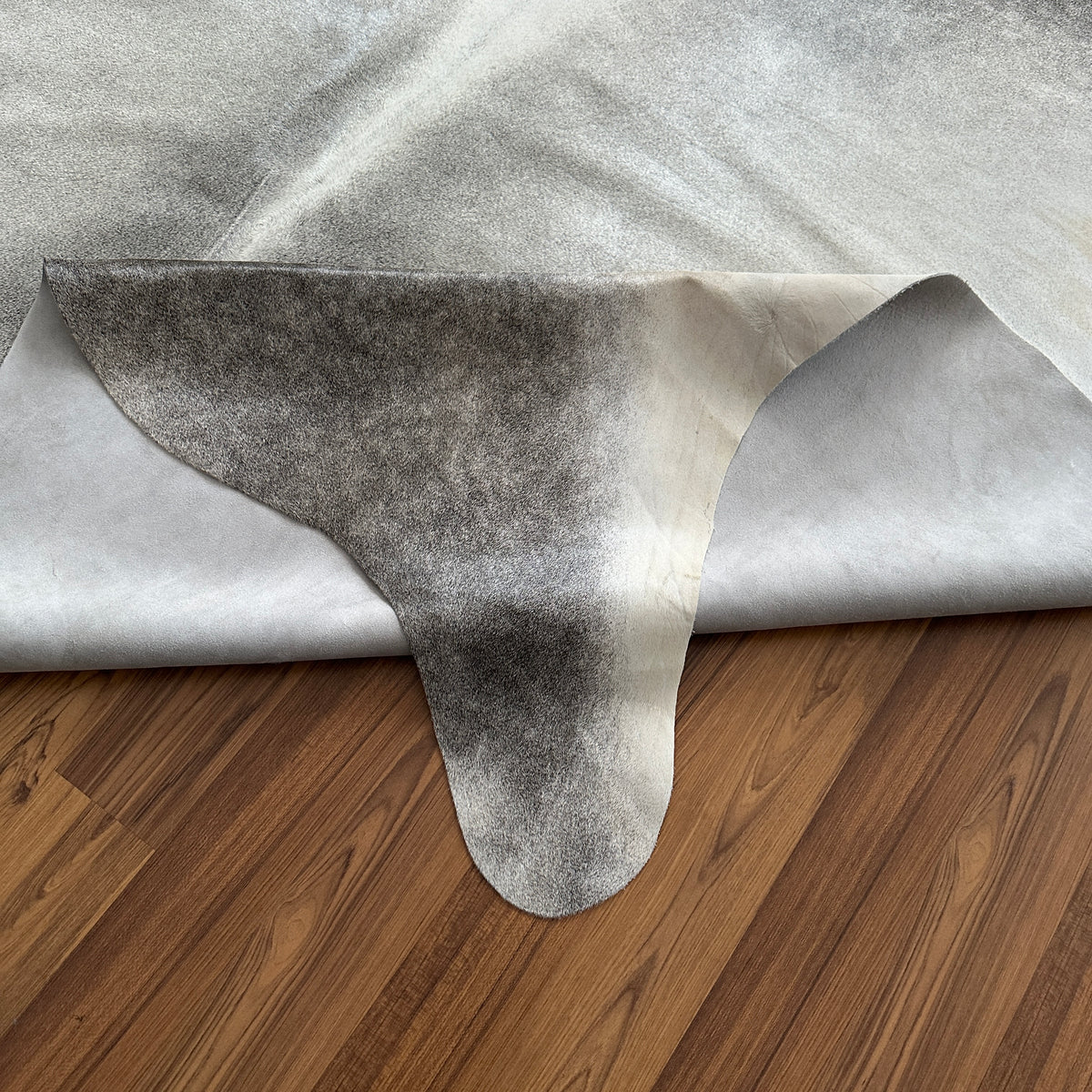 Close-up texture of Grey cowhide rug — Large irregular patches transitioning from charcoal to light grey over cream base