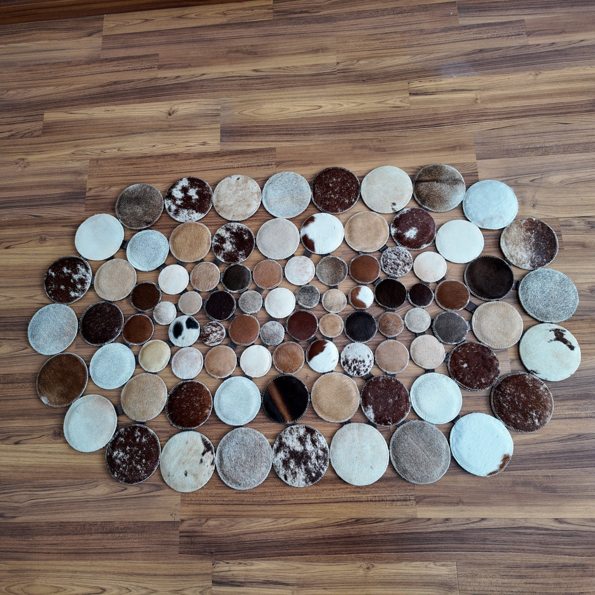 Mixed Tones round patchwork cowhide rug, full overhead view — Assembled circular mosaic of varied hide discs in brown, cream,