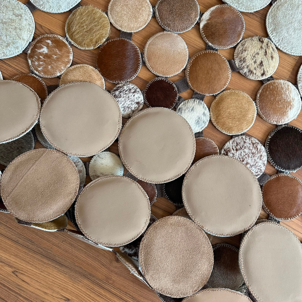 Close-up texture of Mixed Tones round patchwork cowhide rug — Small hide discs in cream, beige, tan, and brown tones arranged