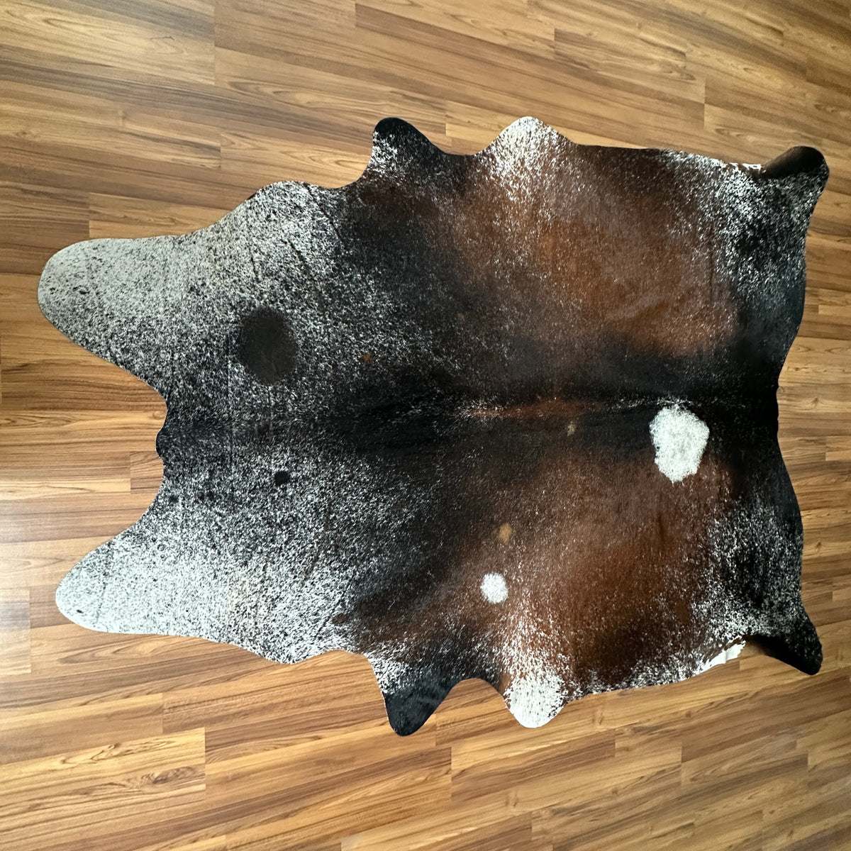 Tricolor tricolor cowhide rug, full overhead view — Irregular patches of dark brown, light grey, and white scattered across n