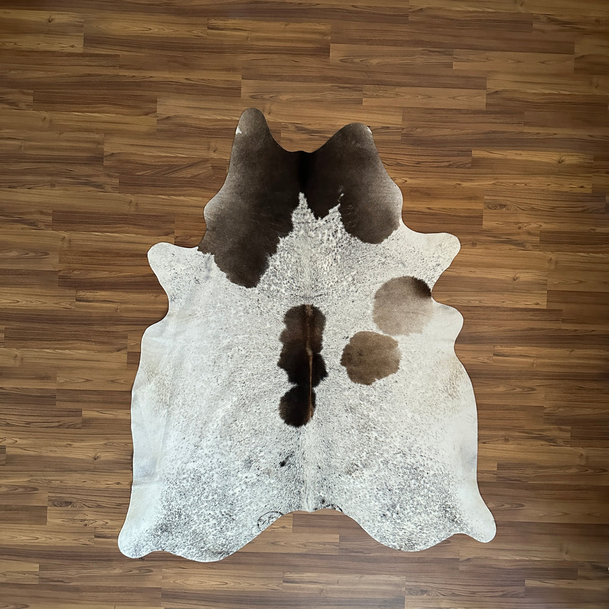 Tricolor tricolor cowhide rug, full overhead view — Large dark brown and black patches on cream and white base with scattered