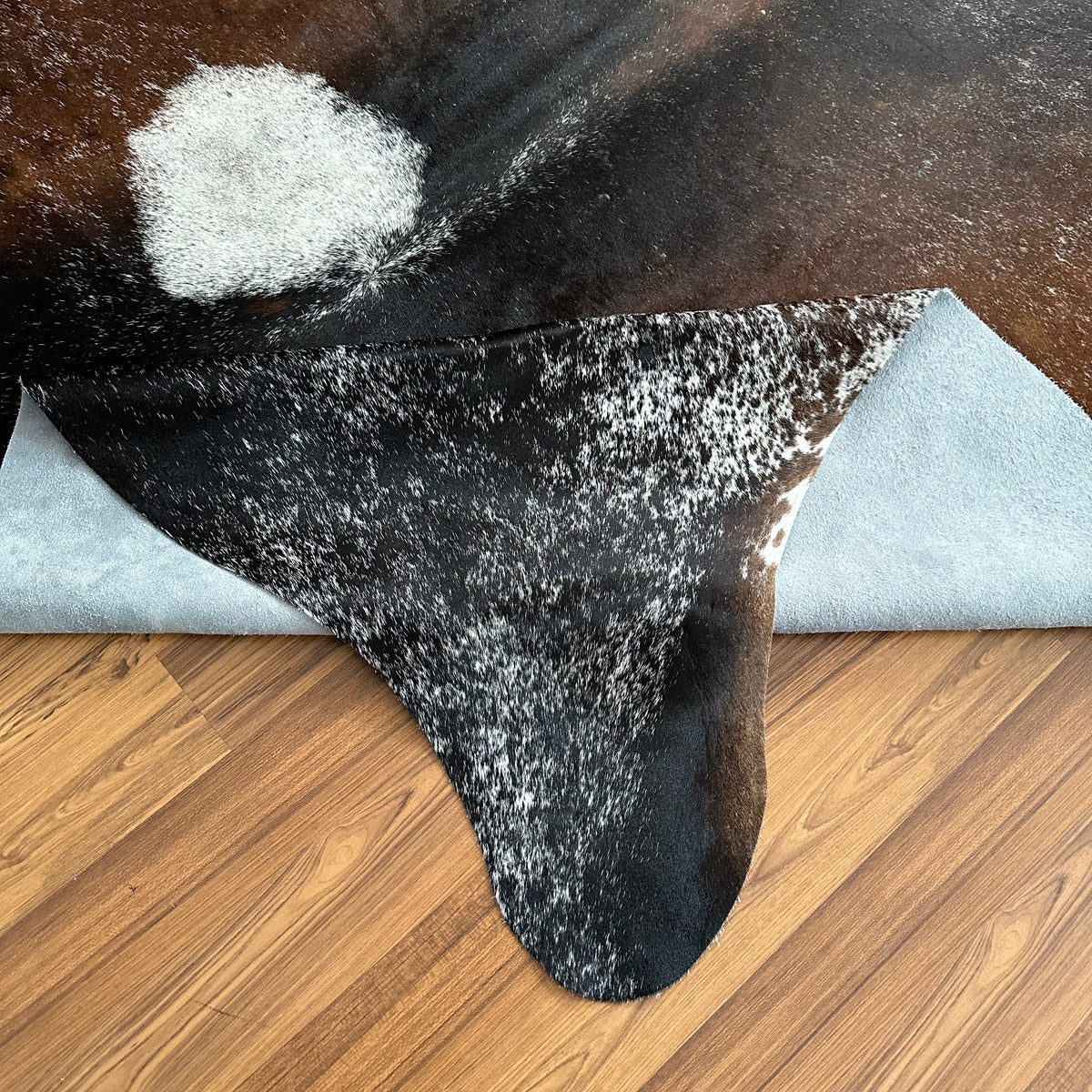 Close-up texture of Tricolor tricolor cowhide rug — Irregular patches of dark brown, light grey, and white scattered across n